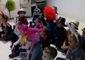Grupa dzieci ubrana w różne rekwizyty pozuje do zdjęcia pamiątkowego na siedząco.